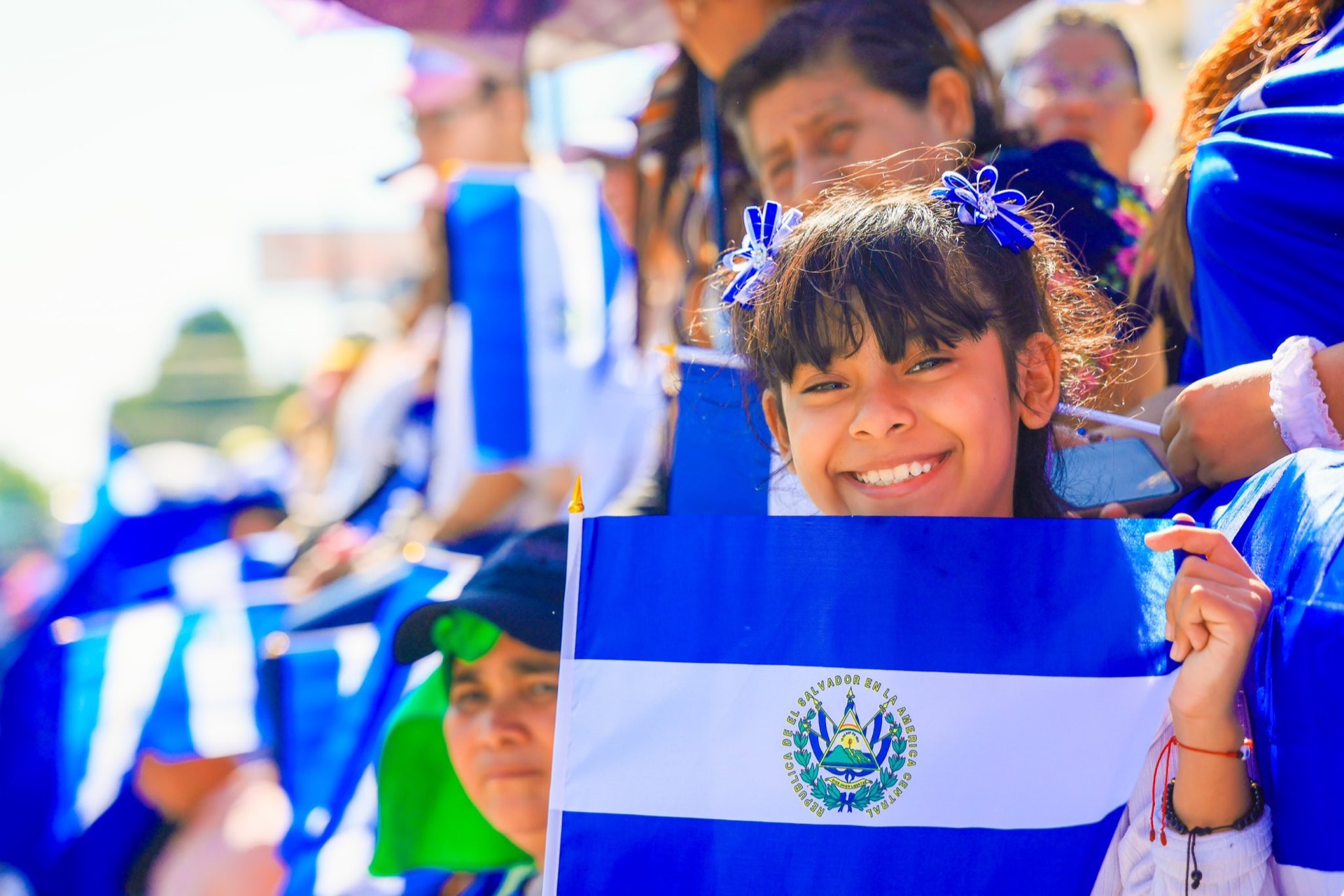Nina sonriendo con la bandera de El Salvador en un desfile del Dia de la Independencia